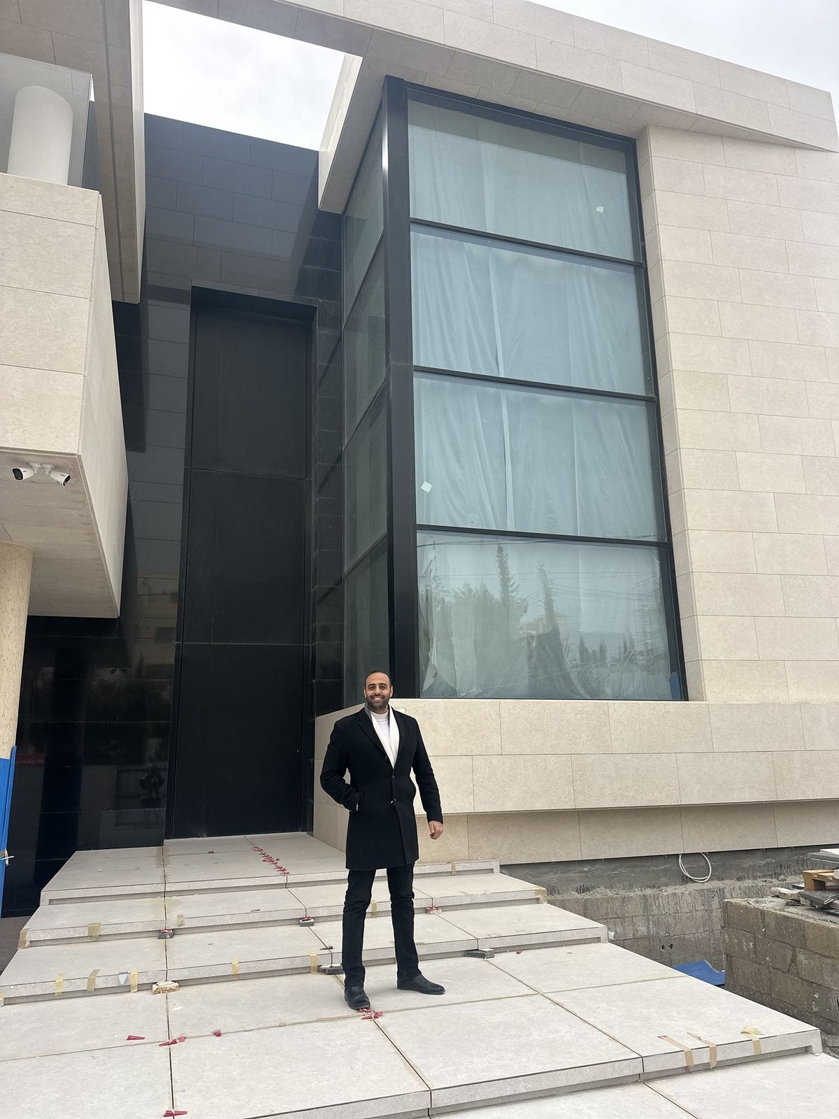 Eng. Faisal Abu Hammour in front of a double-height glass and stone villa facade